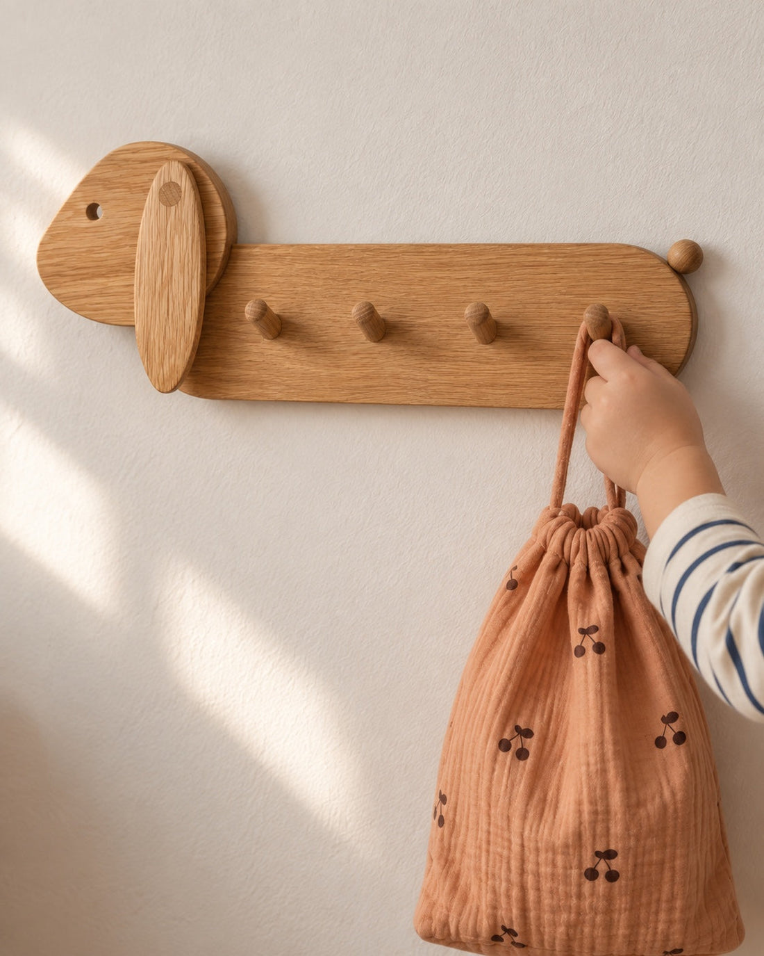 Je le fais tout seul. Gros plan sur la main d’un enfant qui accroche un sac à une patère du modèle lapin.