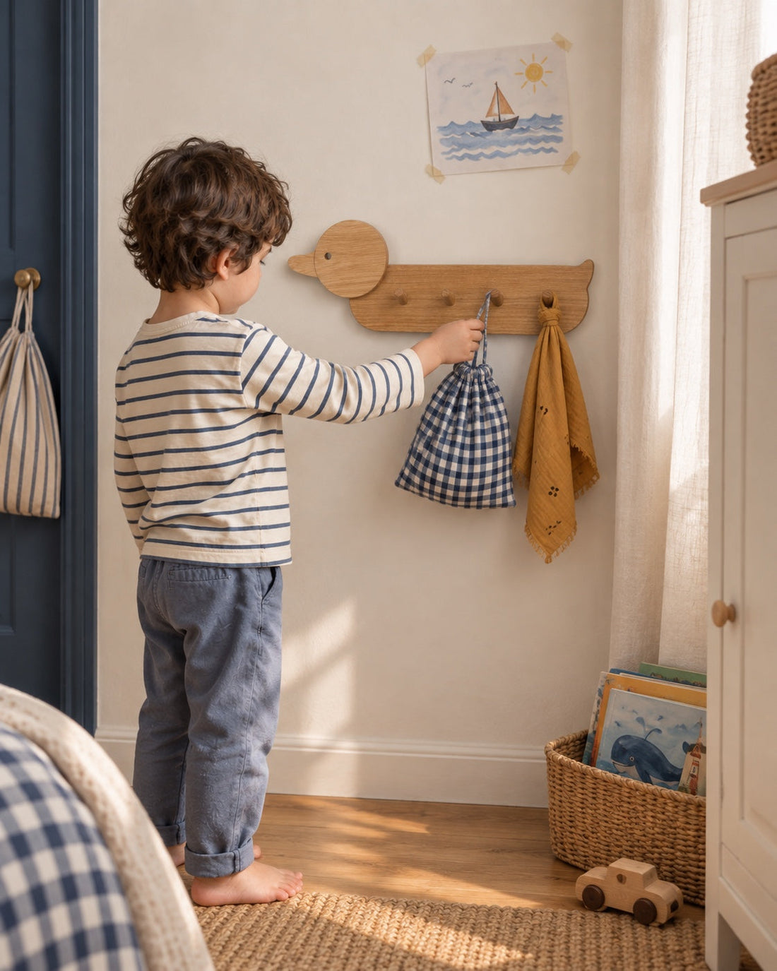 Ses habitudes, à sa hauteur. Un enfant range son sac en tissu sur le porte-manteaux canard, près de ses livres et de ses dessins.
