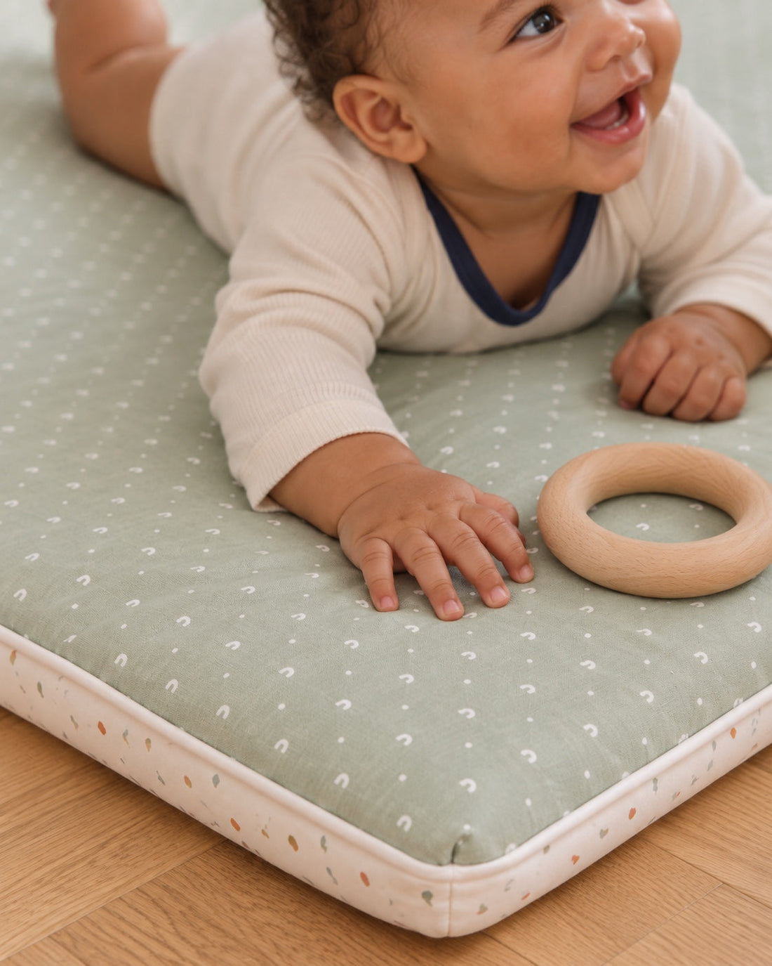 À portée de ses petites mains. Gros plan sur la main du bébé, le tissu sauge et le bord du tapis pendant le jeu.